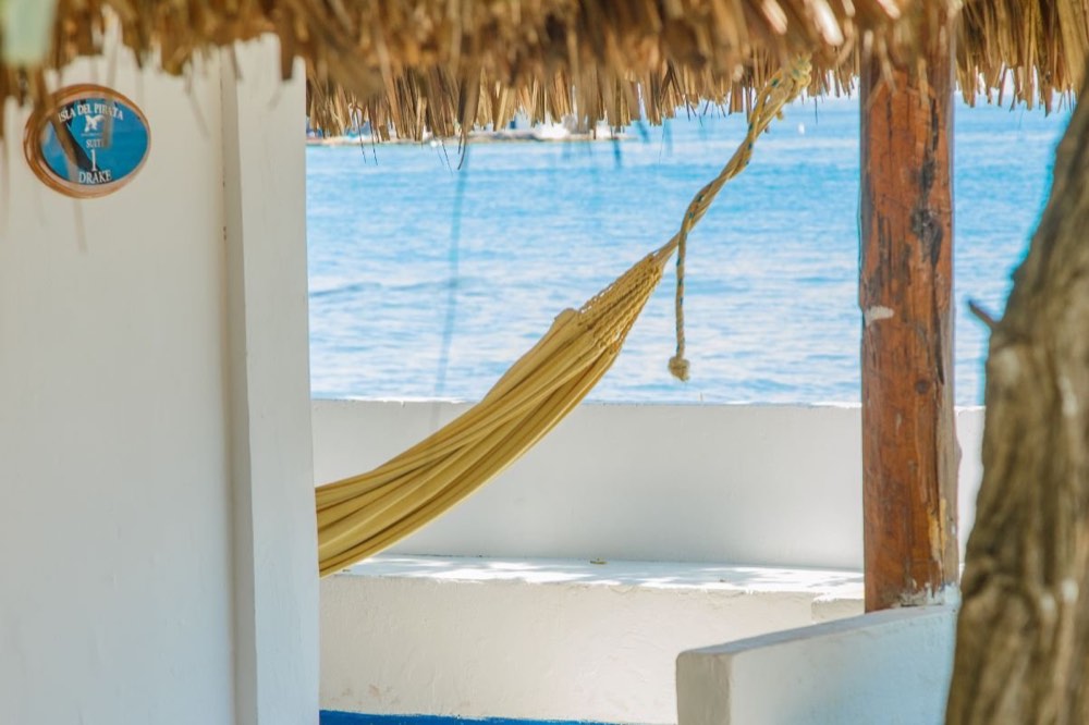 A hammock strung under a thatched roof looking straight out at the turquoise Caribbean